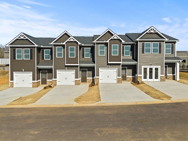 townhome / multi-family property featuring driveway, stone siding, french doors, board and batten siding, and a garage