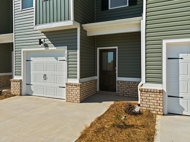 view of exterior entry with a garage, brick siding, and driveway