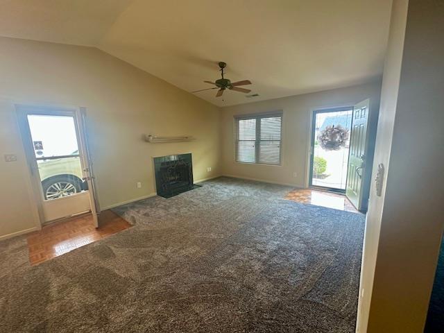 unfurnished living room featuring carpet, baseboards, a fireplace with flush hearth, ceiling fan, and vaulted ceiling