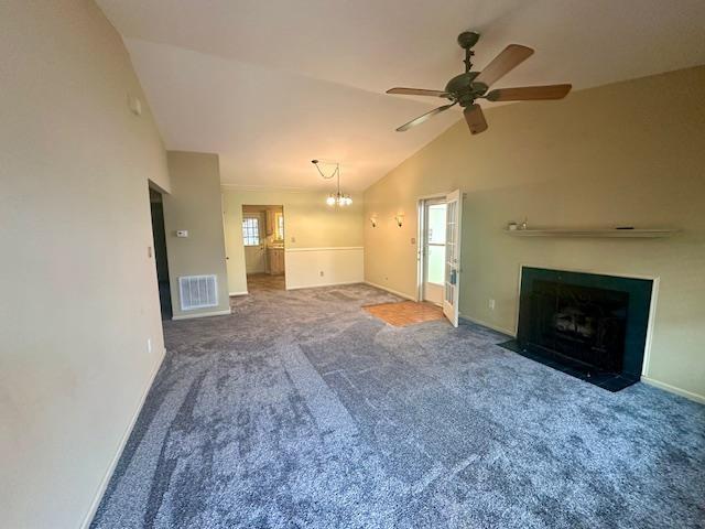 unfurnished living room featuring visible vents, carpet floors, a fireplace with flush hearth, vaulted ceiling, and ceiling fan with notable chandelier