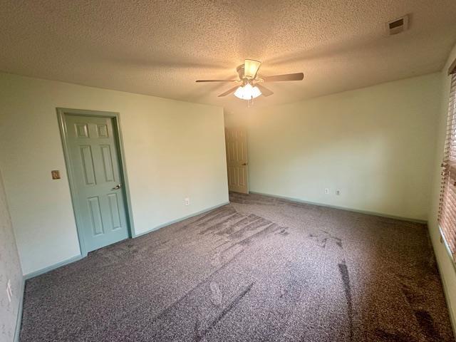 carpeted empty room with a textured ceiling, baseboards, visible vents, and ceiling fan