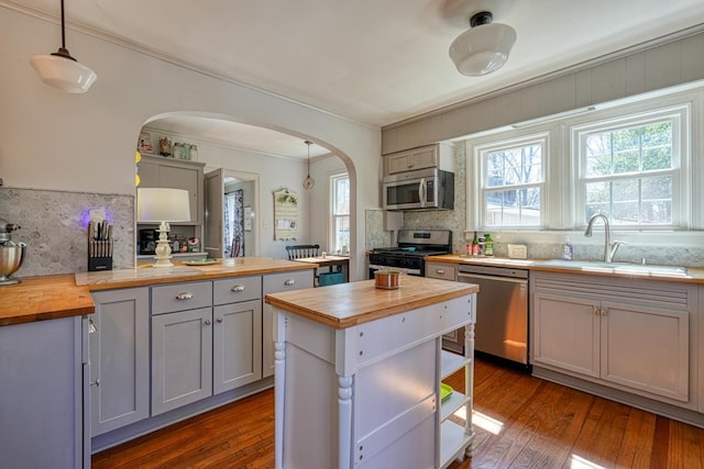 kitchen with gray cabinets, arched walkways, a sink, stainless steel appliances, and butcher block counters