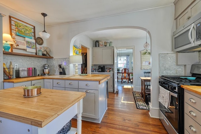 kitchen featuring arched walkways, butcher block counters, stainless steel appliances, and ornamental molding