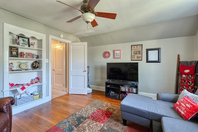 living room featuring built in shelves, baseboards, ceiling fan, and wood finished floors