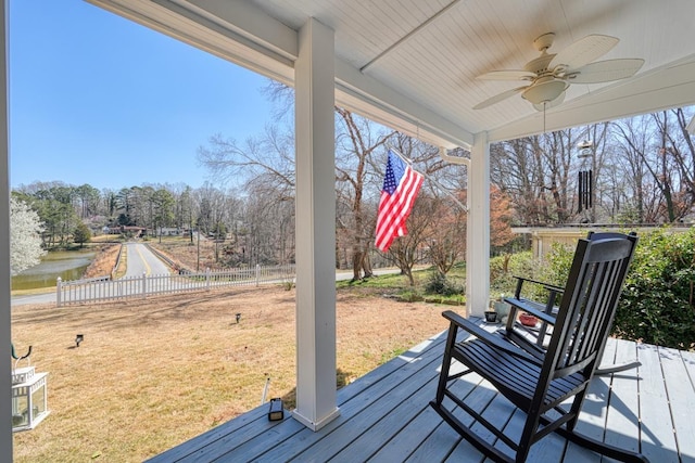 wooden terrace with a yard, a water view, a ceiling fan, and fence