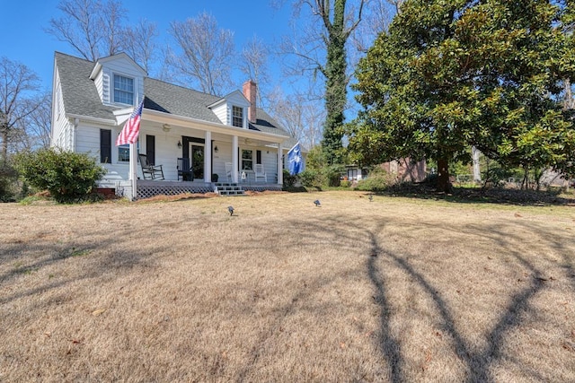 view of front of home featuring a chimney, covered porch, a shingled roof, and a front yard