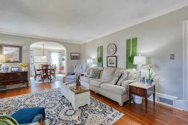 living room with visible vents, crown molding, baseboards, wood finished floors, and arched walkways