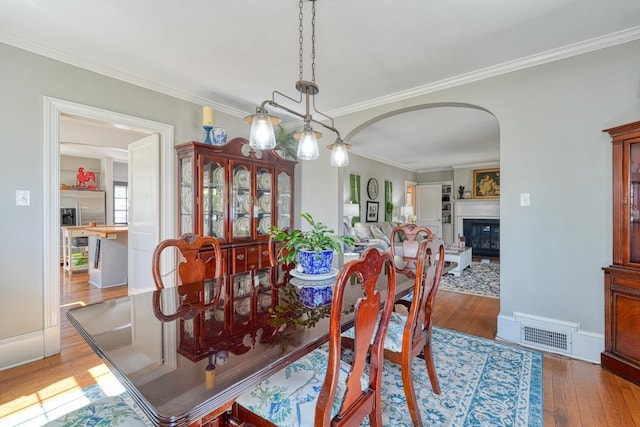 dining room featuring hardwood / wood-style floors, visible vents, arched walkways, ornamental molding, and a glass covered fireplace