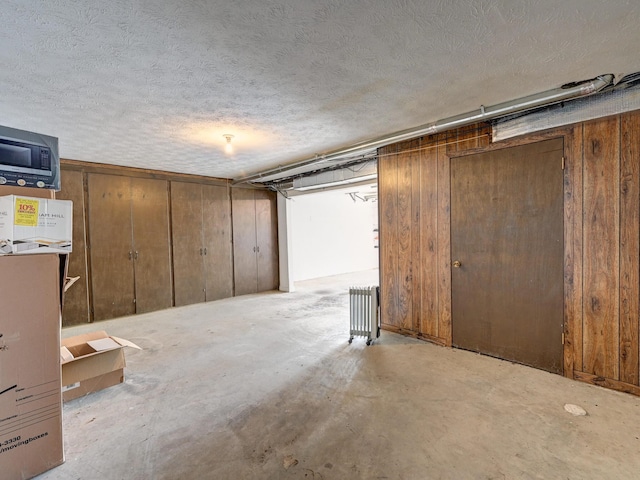 below grade area with radiator, wood walls, and a textured ceiling