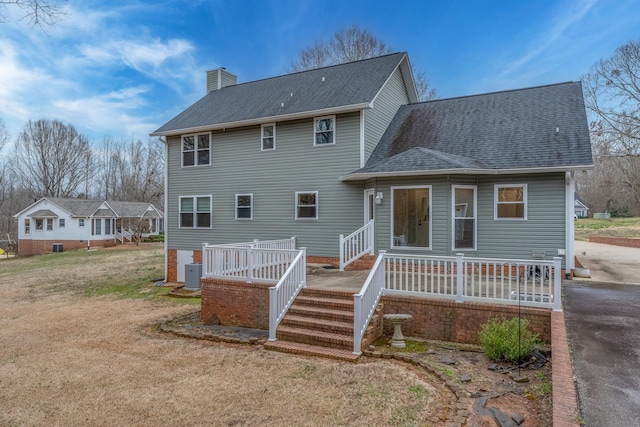 rear view of property featuring a shingled roof, central air condition unit, and a chimney