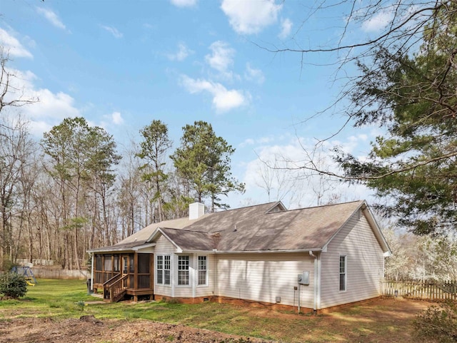 back of house with fence, roof with shingles, a yard, a sunroom, and a chimney