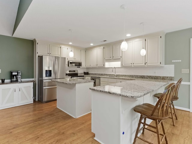 kitchen featuring light stone countertops, a peninsula, light wood-style flooring, stainless steel appliances, and decorative backsplash