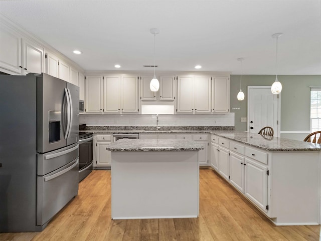 kitchen with a sink, stainless steel appliances, a peninsula, light wood finished floors, and decorative backsplash