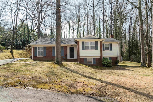 tri-level home with brick siding, a chimney, and a front yard