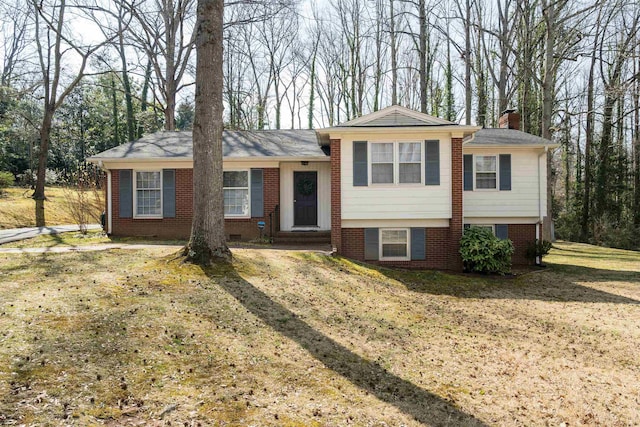 split level home with brick siding, a chimney, and a front lawn