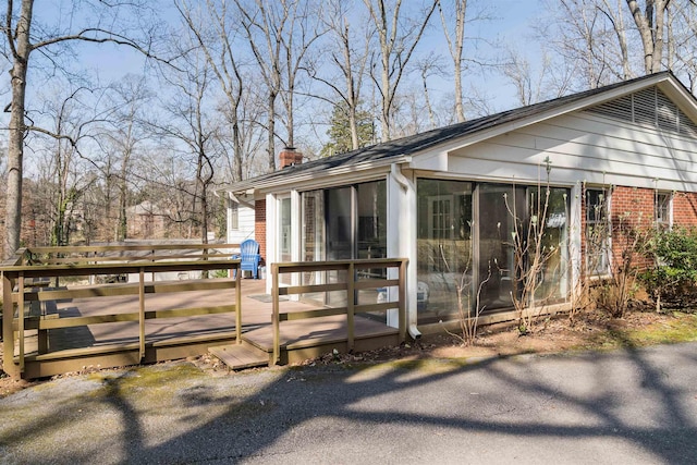 view of side of home featuring a wooden deck, brick siding, a chimney, and a sunroom