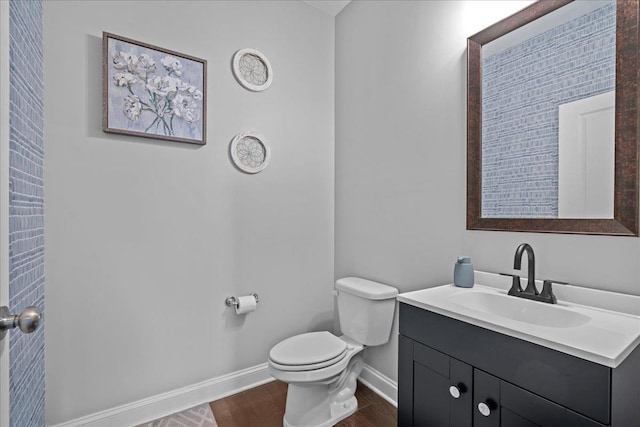 half bath with toilet, vanity, baseboards, and wood finished floors