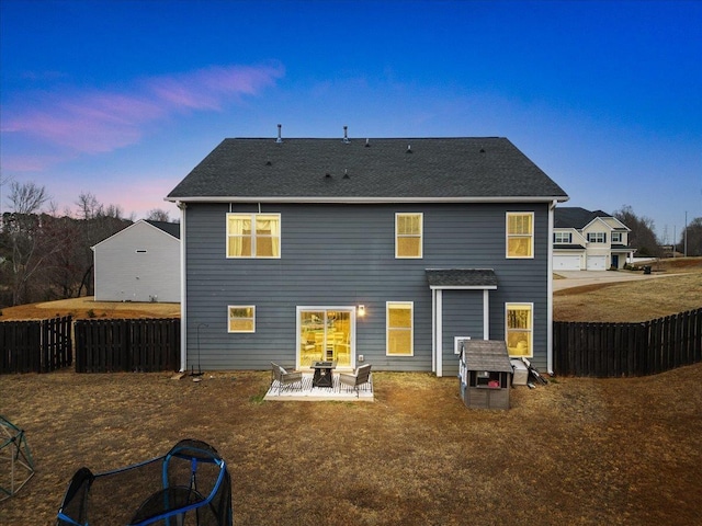 back of house at dusk with roof with shingles, a patio, and fence