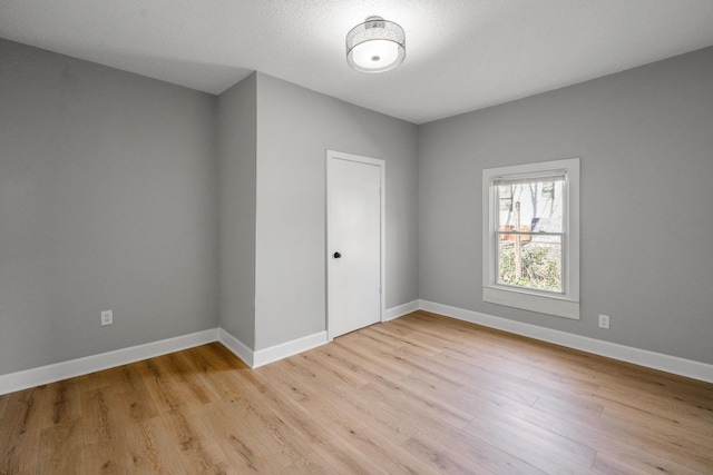 spare room with light wood-style flooring, a textured ceiling, and baseboards