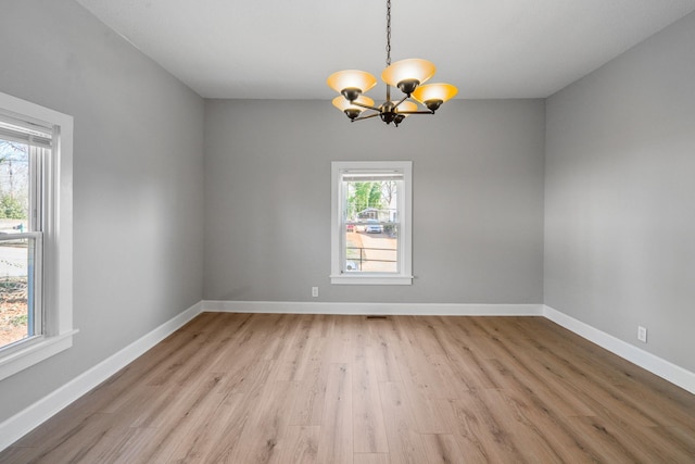 empty room with light wood-style floors, an inviting chandelier, a healthy amount of sunlight, and baseboards