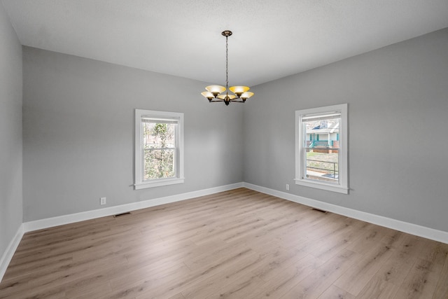 unfurnished room featuring an inviting chandelier, light wood-style floors, visible vents, and baseboards