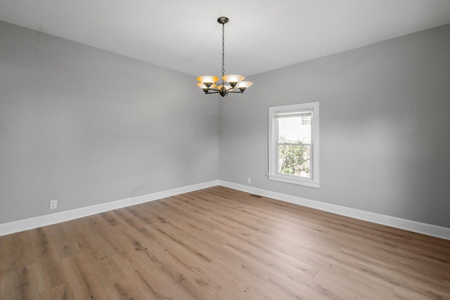 empty room with a chandelier, visible vents, baseboards, and wood finished floors