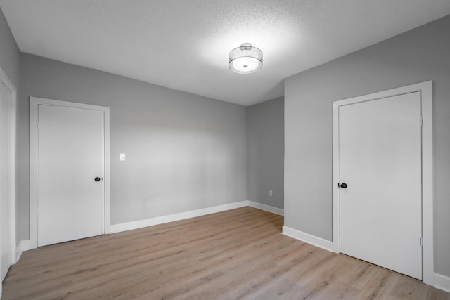 empty room featuring baseboards, a textured ceiling, and light wood finished floors