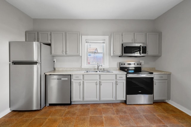 kitchen with gray cabinets, a sink, stainless steel appliances, light countertops, and baseboards