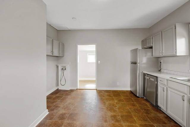 kitchen featuring baseboards, a sink, light countertops, stone finish floor, and dishwasher