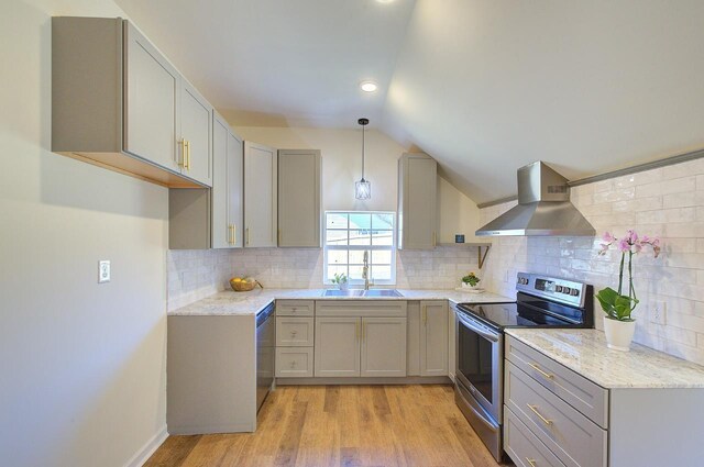 kitchen featuring gray cabinets, a sink, vaulted ceiling, appliances with stainless steel finishes, and wall chimney exhaust hood