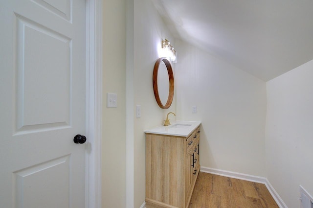 bathroom with visible vents, baseboards, vaulted ceiling, wood finished floors, and vanity