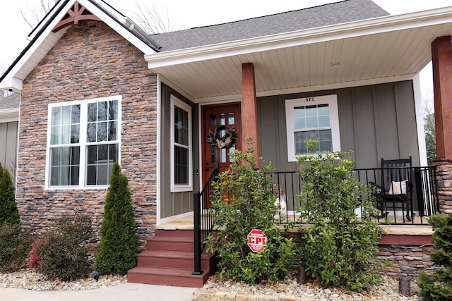 doorway to property with stone siding, a porch, a shingled roof, and board and batten siding