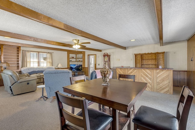 dining area featuring ceiling fan, beamed ceiling, wood walls, and a textured ceiling