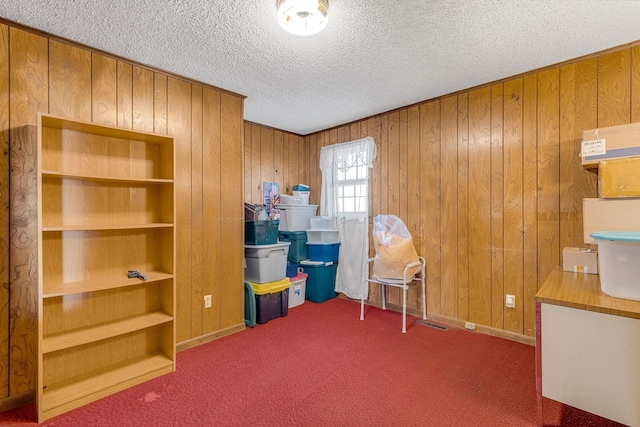 unfurnished office with carpet floors, built in shelves, wood walls, and a textured ceiling