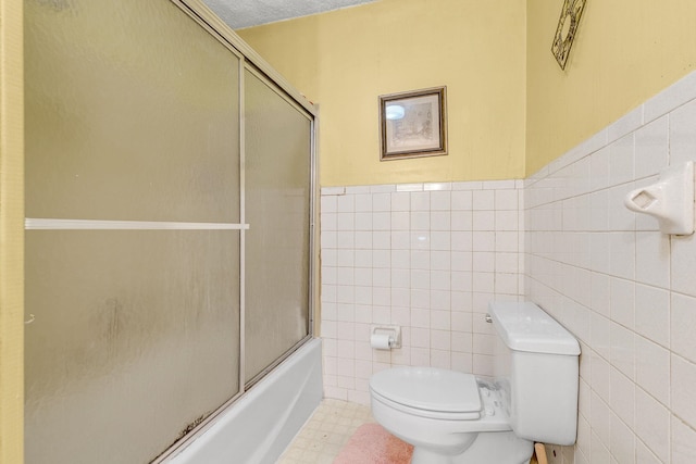 full bath with wainscoting, combined bath / shower with glass door, toilet, and tile walls