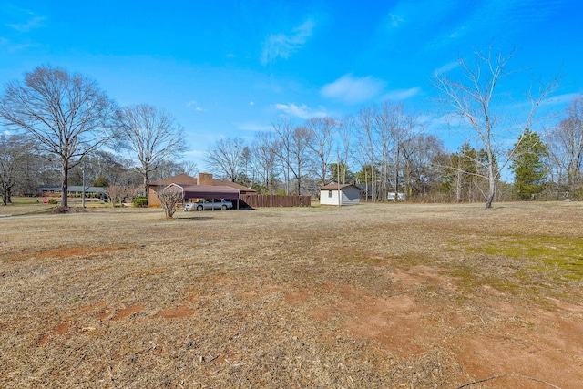 view of yard featuring a carport, fence, and an outbuilding