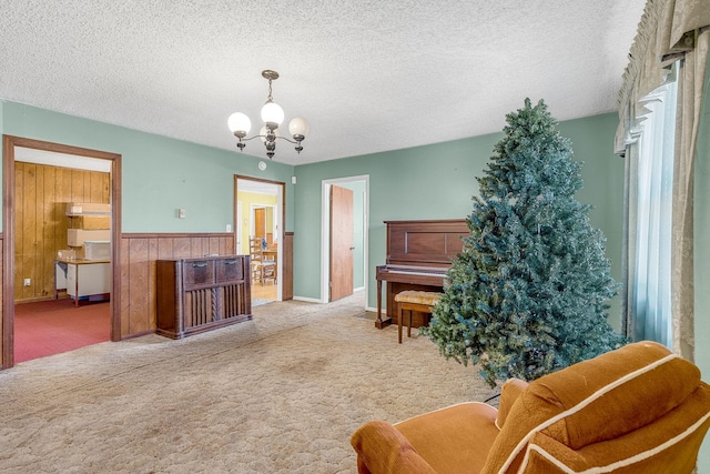 sitting room with a textured ceiling, carpet, an inviting chandelier, wood walls, and wainscoting