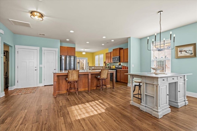 kitchen with visible vents, brown cabinetry, a center island with sink, and stainless steel appliances