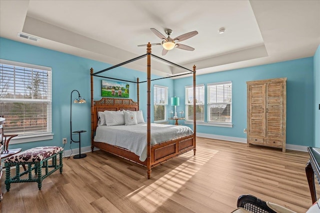 bedroom with a tray ceiling, wood finished floors, visible vents, and baseboards