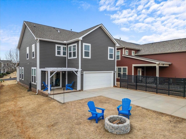 back of property featuring driveway, an outdoor fire pit, an attached garage, a shingled roof, and a patio area