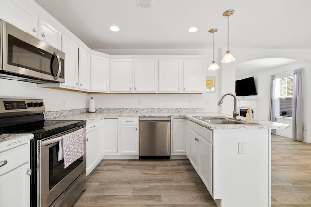 kitchen with a peninsula, stainless steel appliances, light wood-type flooring, and a sink