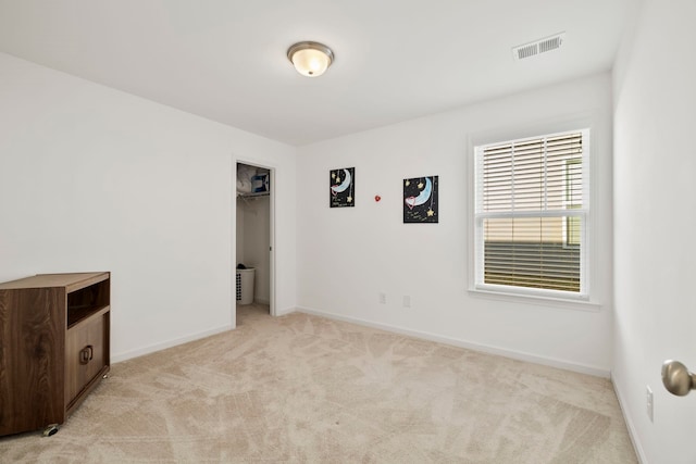 unfurnished bedroom with visible vents, light colored carpet, a walk in closet, and baseboards