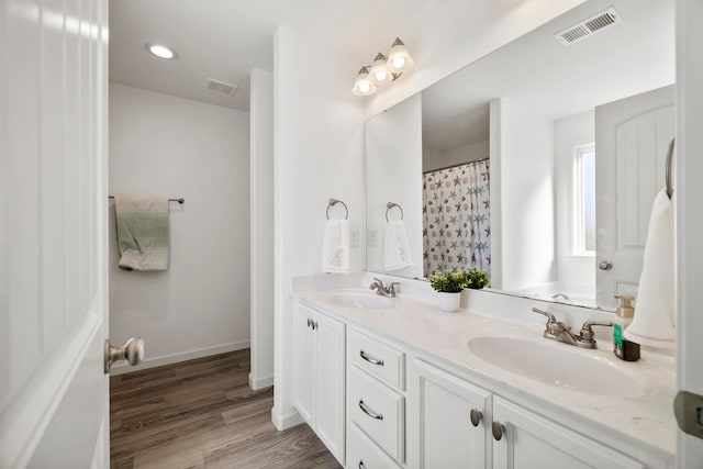 full bathroom featuring double vanity, visible vents, wood finished floors, and a sink