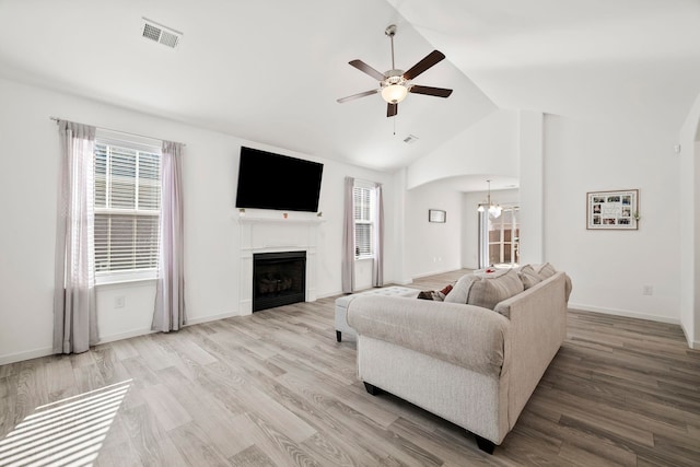 living room with vaulted ceiling, ceiling fan with notable chandelier, visible vents, and light wood finished floors