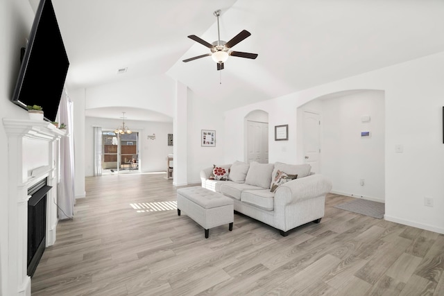 living room with baseboards, light wood-type flooring, ceiling fan with notable chandelier, a fireplace, and arched walkways