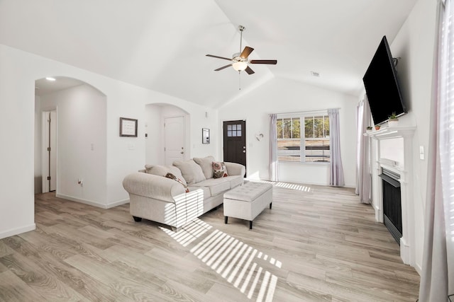 living room featuring a fireplace, a ceiling fan, arched walkways, and light wood-type flooring