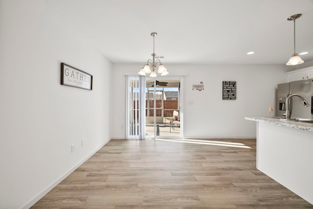 unfurnished dining area with an inviting chandelier, light wood-style floors, baseboards, and a sink