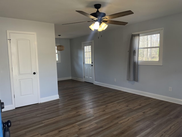 spare room featuring a healthy amount of sunlight, a ceiling fan, baseboards, and dark wood-style flooring