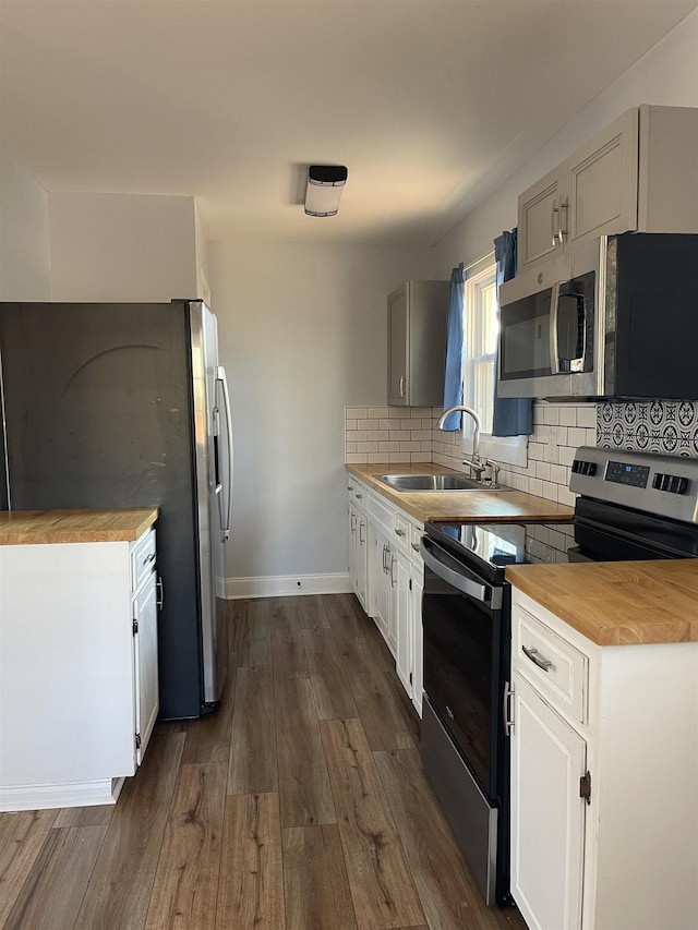 kitchen with dark wood-style floors, a sink, decorative backsplash, butcher block countertops, and stainless steel appliances