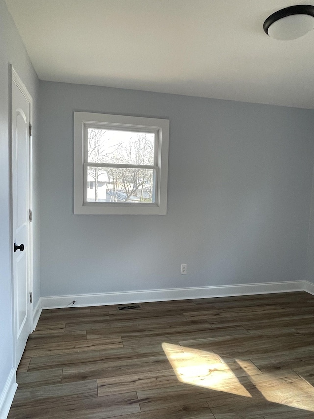 unfurnished room featuring dark wood-style floors, visible vents, and baseboards